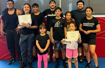 Cassandra Samel in wrestling gear posing on the mat at Adrenaline MMA & Fitness, showcasing her skills as a top young wrestler in San Bernardino.